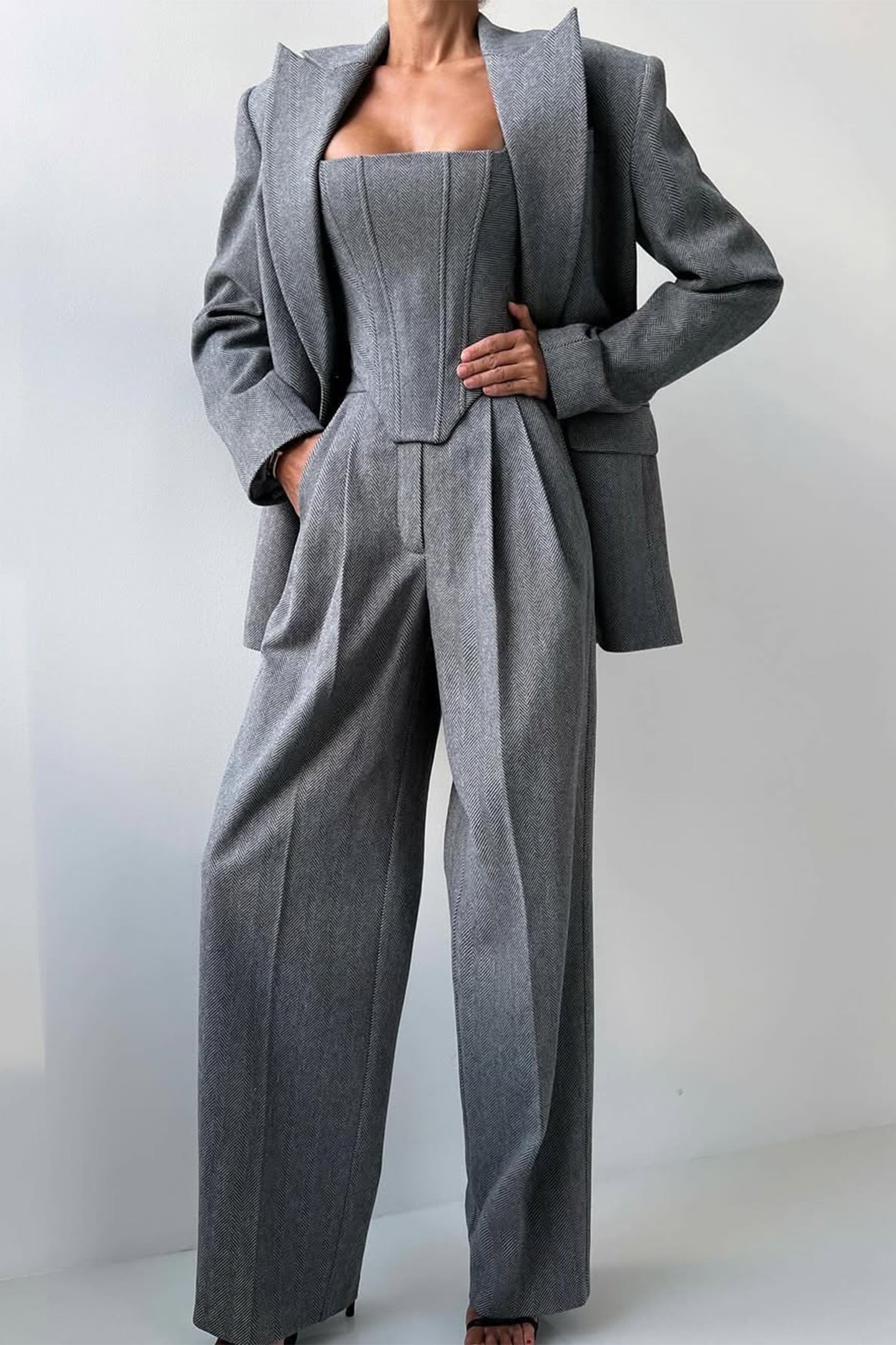 "Elegant women's three-piece suit with structured blazer, bustier top, and wide-leg trousers in classic herringbone weave."