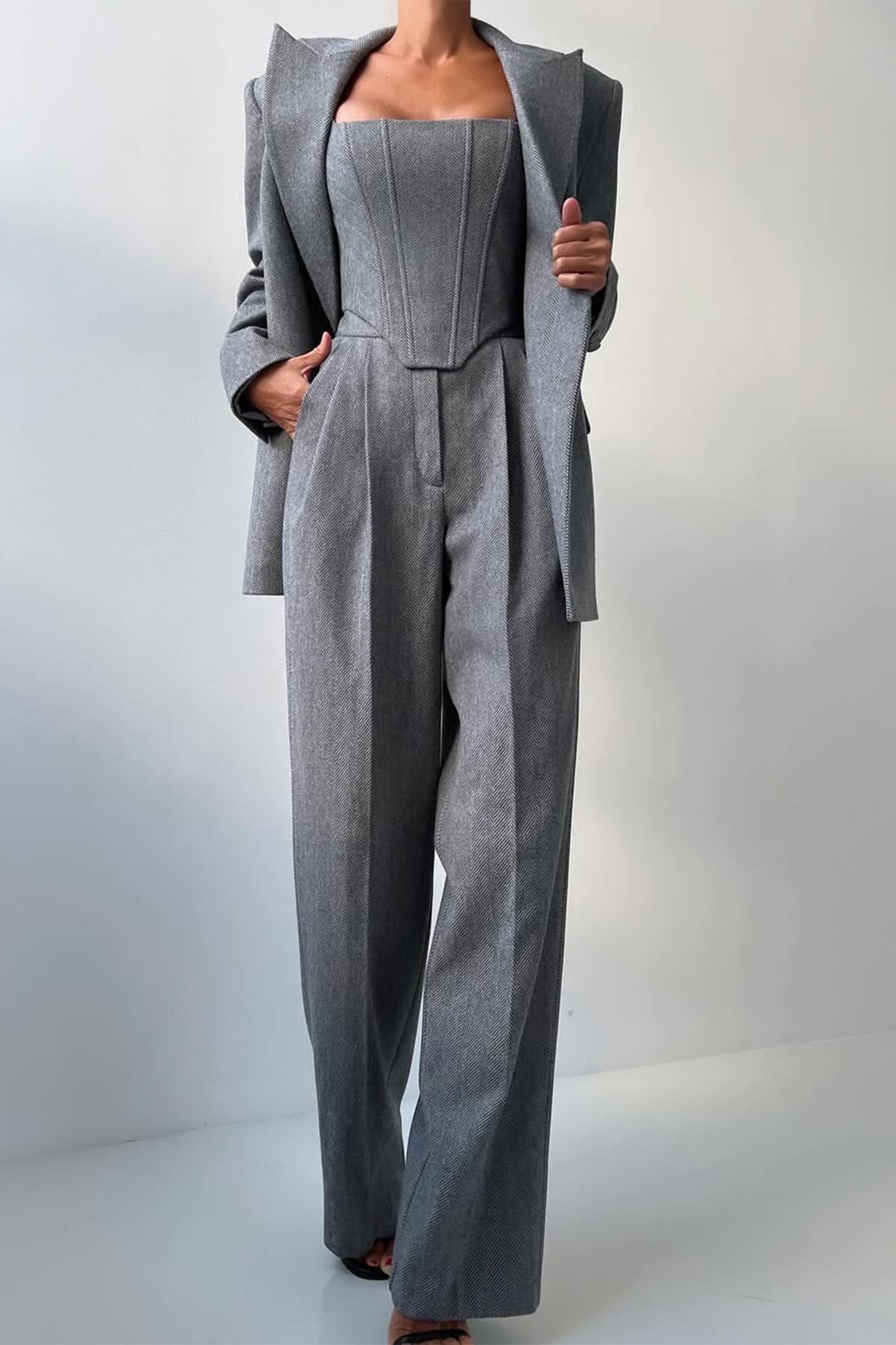 "Elegant women's three-piece suit with structured blazer, bustier top, and wide-leg trousers in classic herringbone weave."