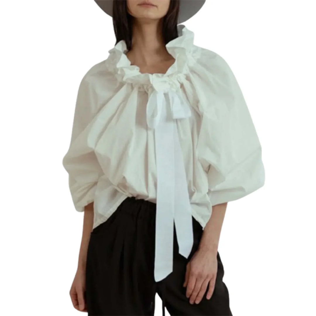 Full-length shot of a women wearing an elegant white blouse with puffed lantern sleeves and bow tie.