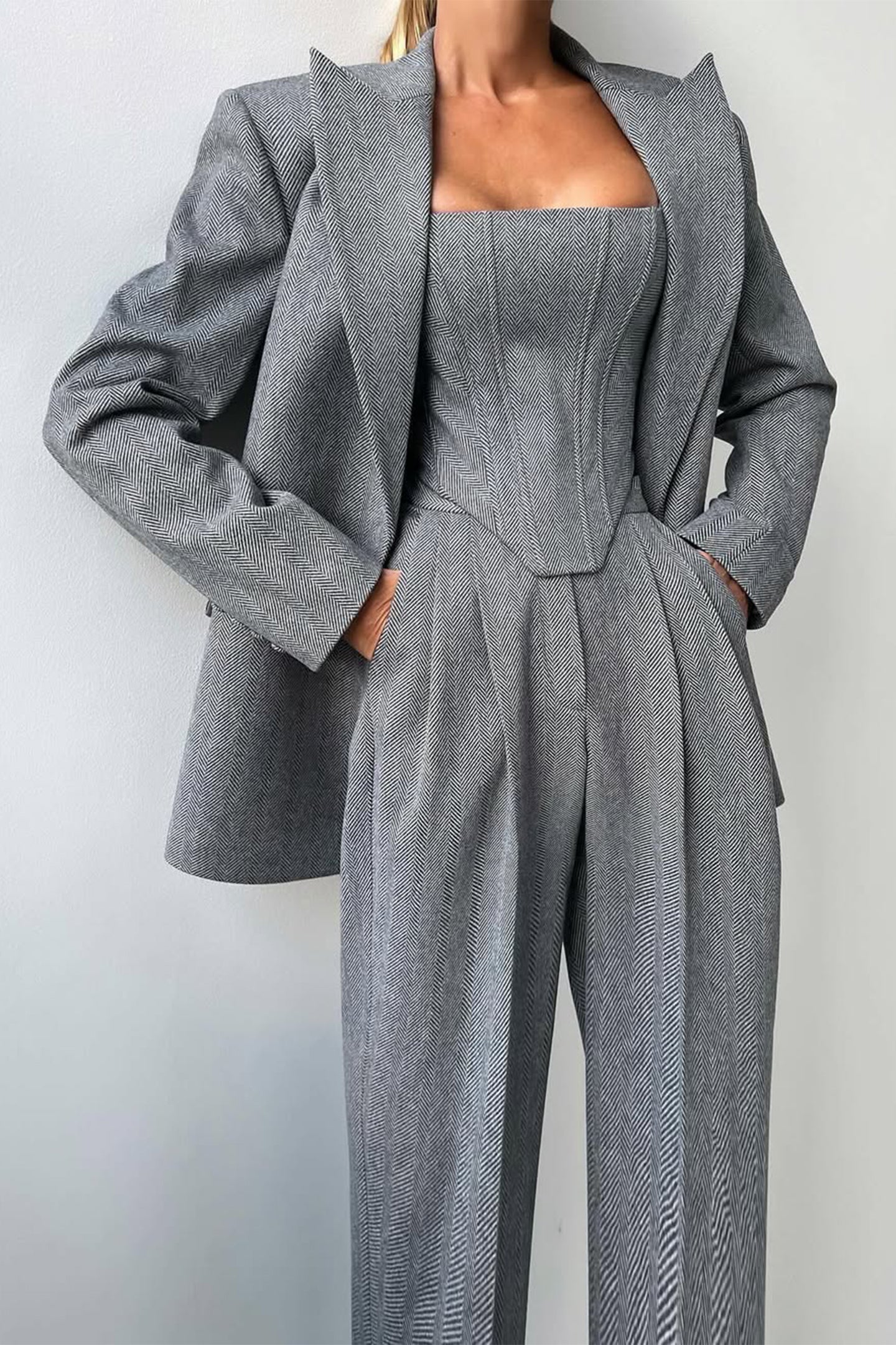 "Elegant women's three-piece suit with structured blazer, bustier top, and wide-leg trousers in classic herringbone weave."