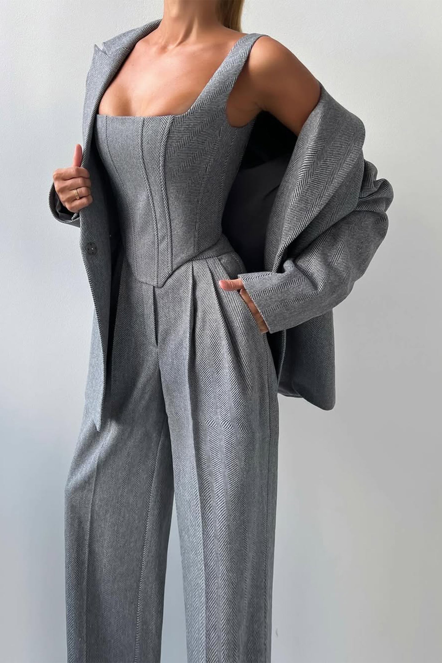 "Elegant women's three-piece suit with structured blazer, bustier top, and wide-leg trousers in classic herringbone weave."