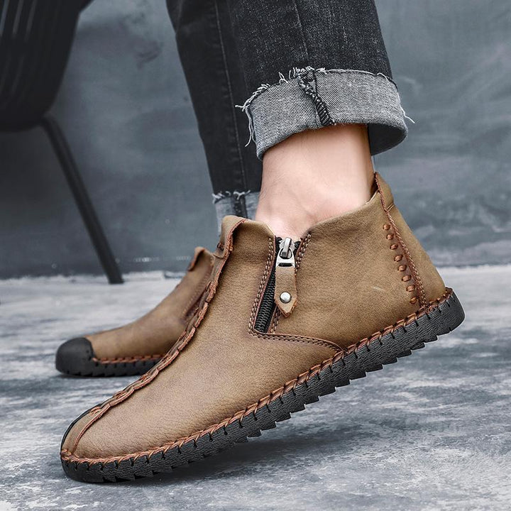 Close-up of hand-stitched detailing on men's brown leather ankle boot, non-slip sole visible