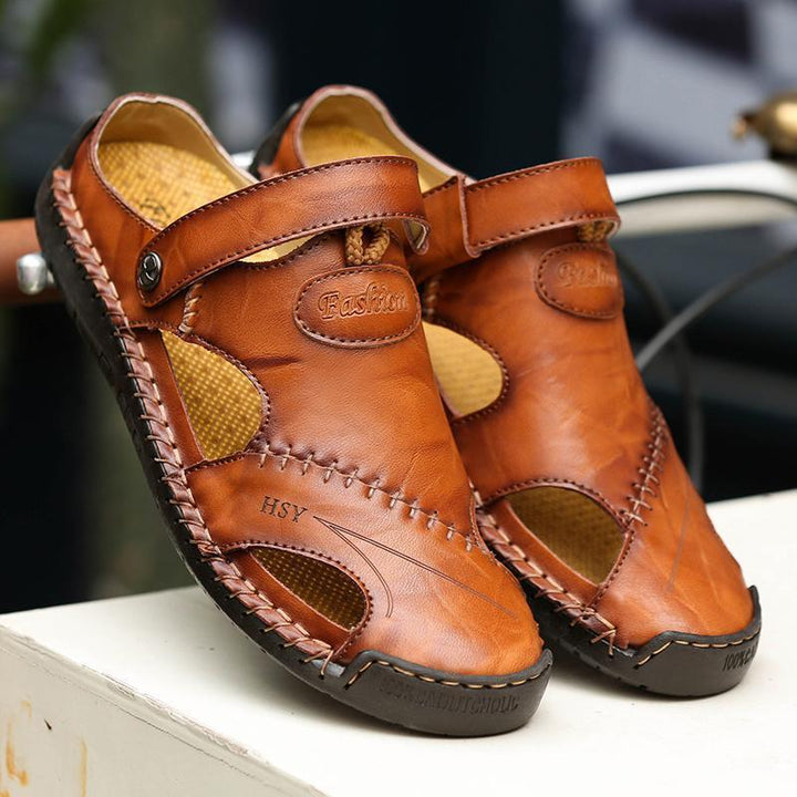 Men's casual leather sandals, closed-toe design, presented on a natural wood surface.