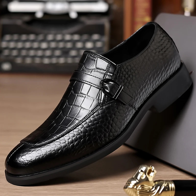 Close-up of a men's luxury leather monk strap loafer, showcasing the detailed crocodile texture and buckle.