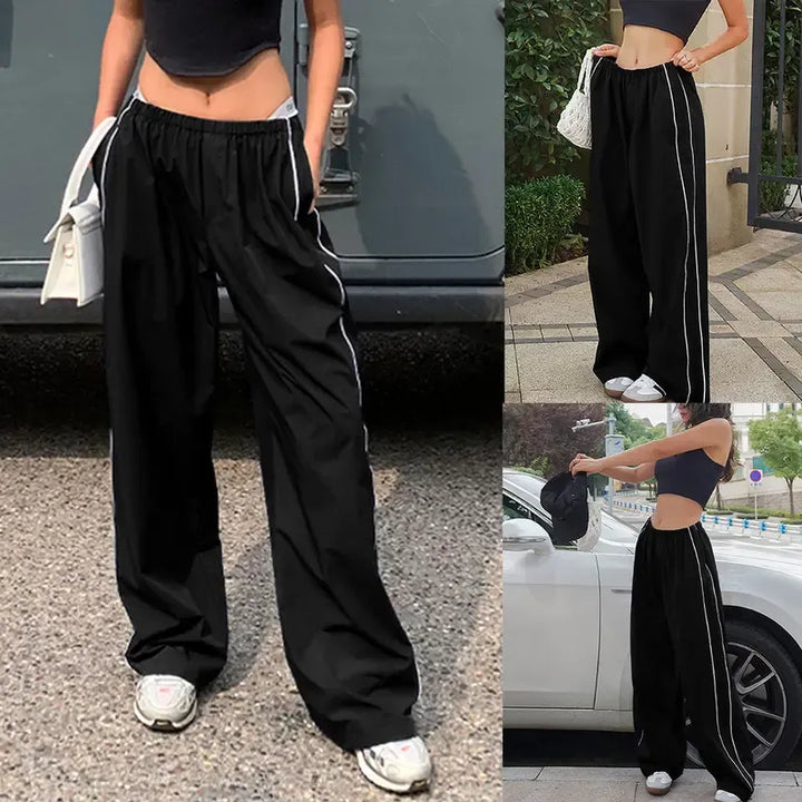 Fashionable women's wide leg track pants in black polyester with sporty contrast piping detail.