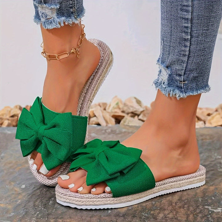 Elegant women's slip-on pearl bow slide sandals. Chic and comfortable flat summer footwear for casual or vacation wear.