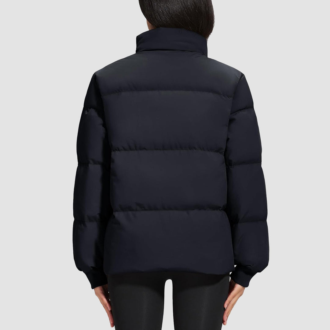 Woman looking at cityscape, bundled in a black lightweight quilted puffer jacket
